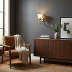 Against a charcoal wall, this matte black Clérachic wall sconce glows above a walnut console beside a leather chair.