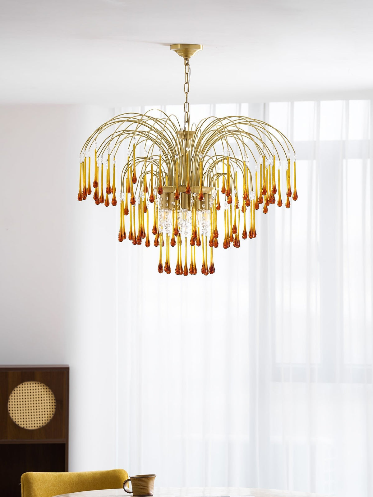 This Clérachic pendant hangs beside a sheer curtain and cane-panelled cabinet, caramel crystal drops catching the light.