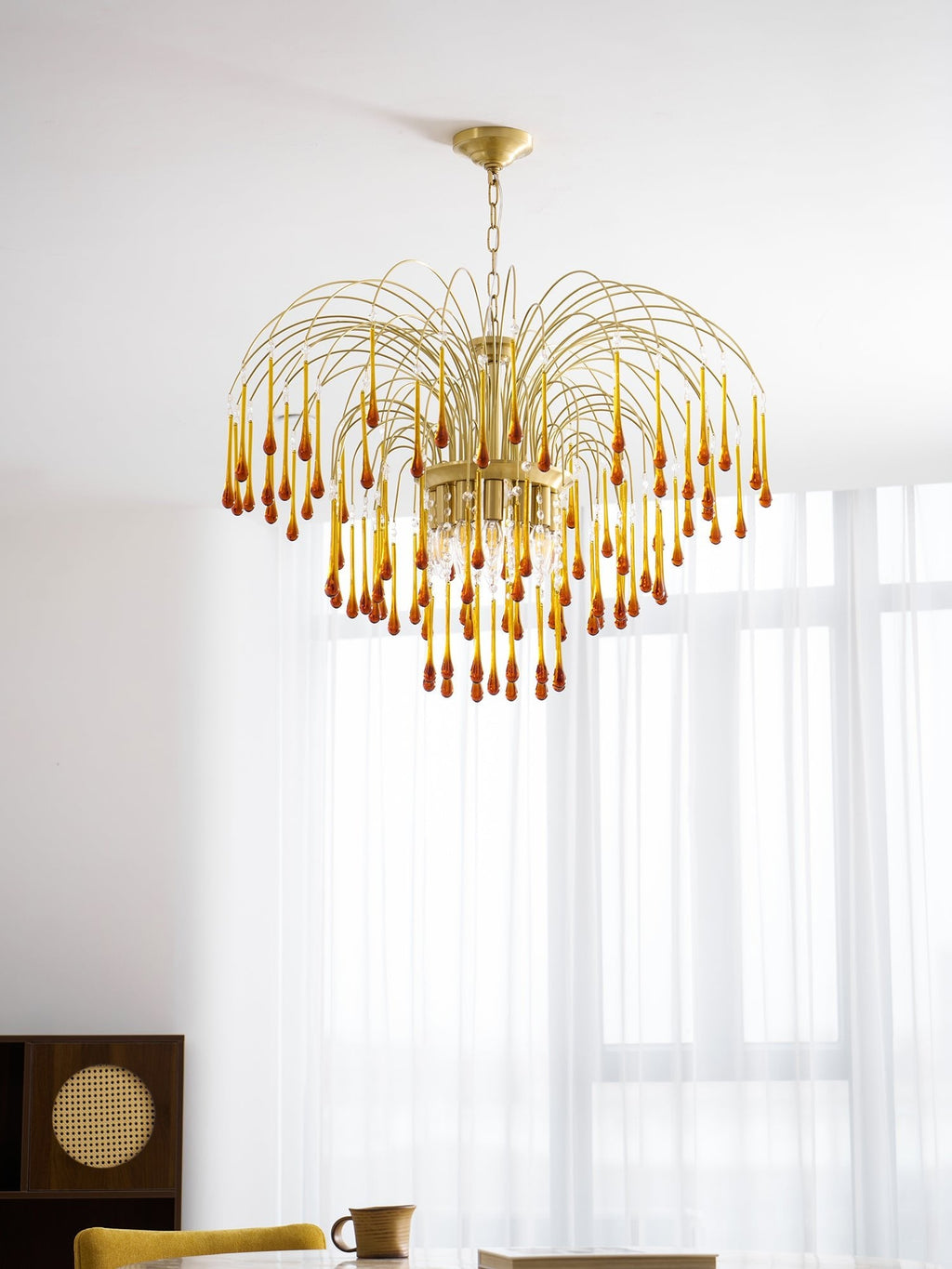 This Clérachic pendant's caramel crystal drops hang near a mustard-yellow chair and a cane-panelled cabinet.