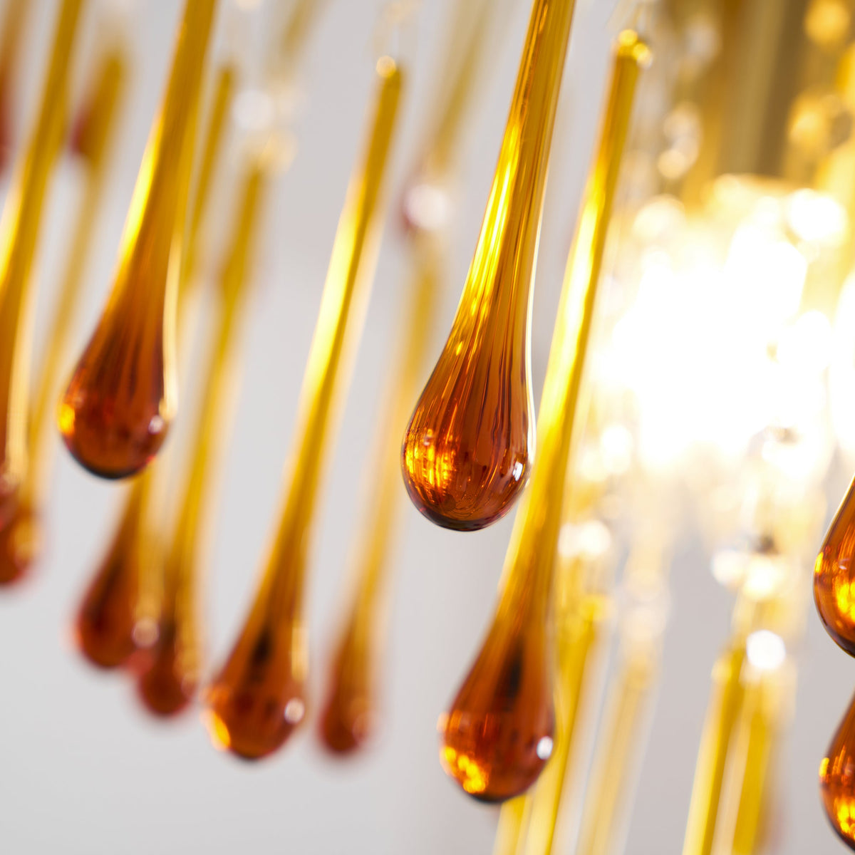 Close view of amber glass teardrops on this Clérachic chandelier, their curved brass stems blurred behind.