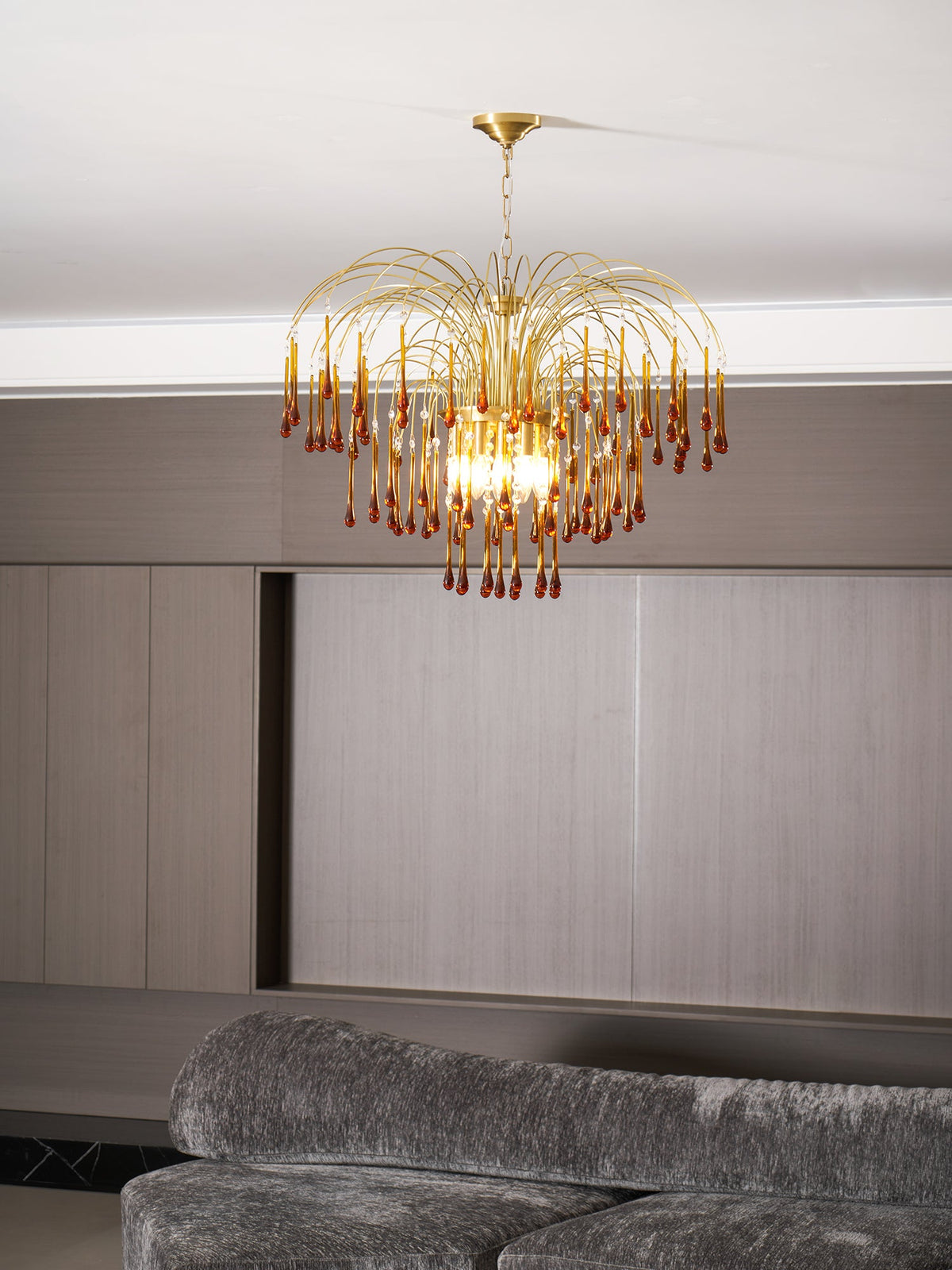 This Clérachic pendant's caramel crystal drops hang above a grey sofa in daylight, pale wood panelling behind.