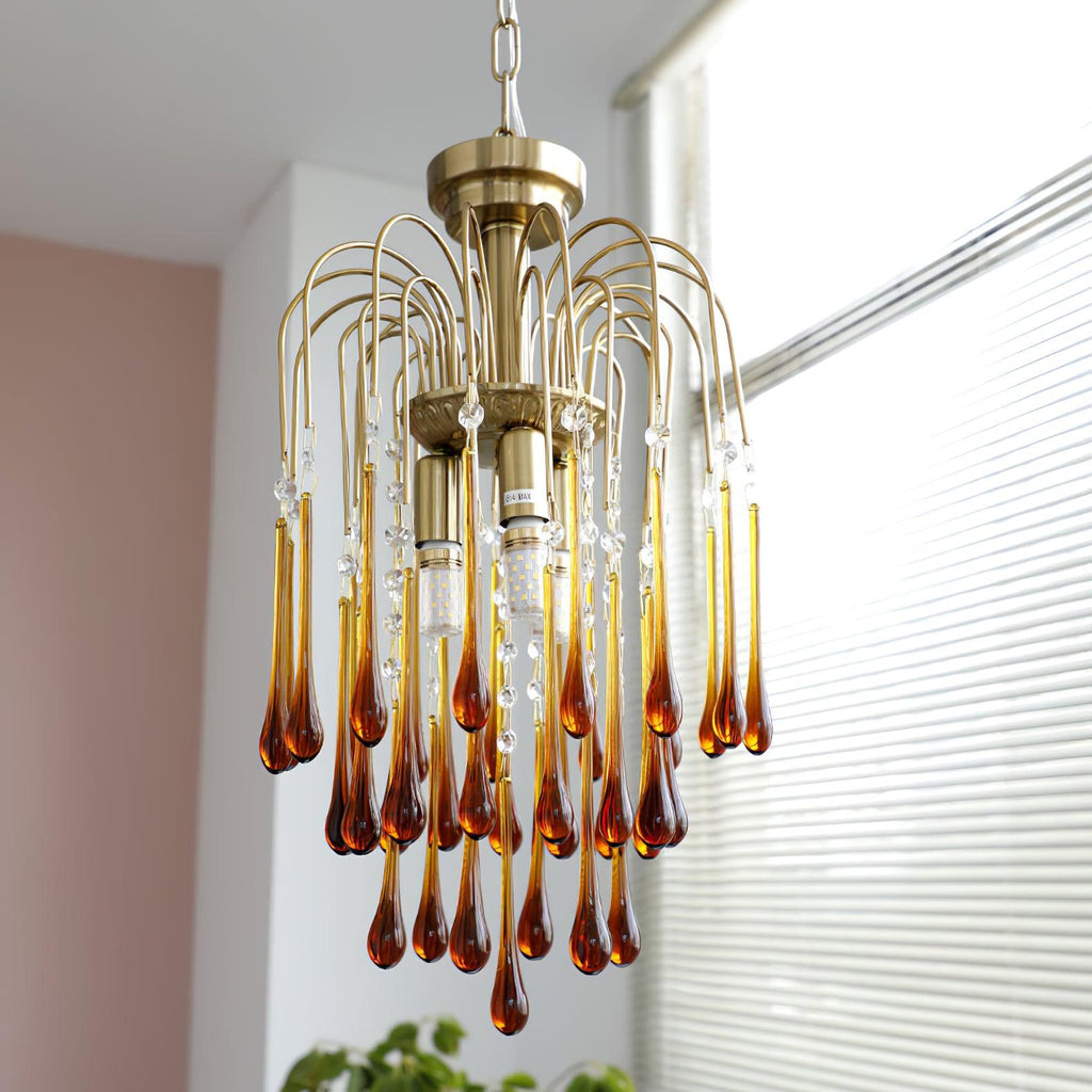 Clear crystal drops hang from this Clérachic pendant's brass arms, shown beside a row of white slatted blinds.