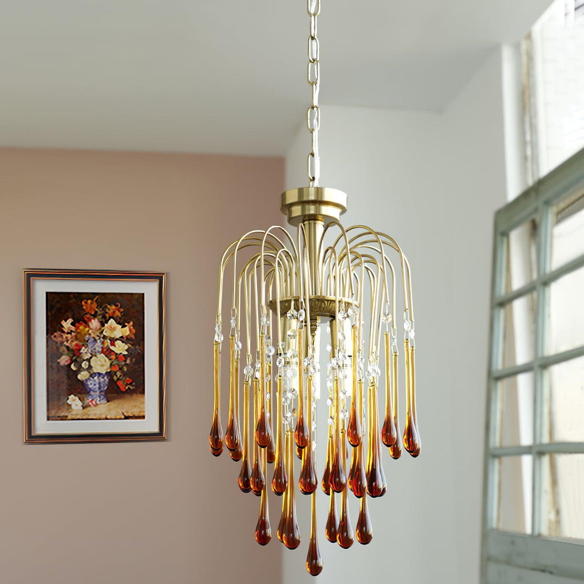 A framed floral picture hangs beside this Clérachic pendant, its caramel crystal drops lit against a soft pink wall.