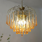 Multiple warm bulbs glow inside this Clérachic chandelier, its caramel crystal drops hanging in a plain room with a hint of greenery.