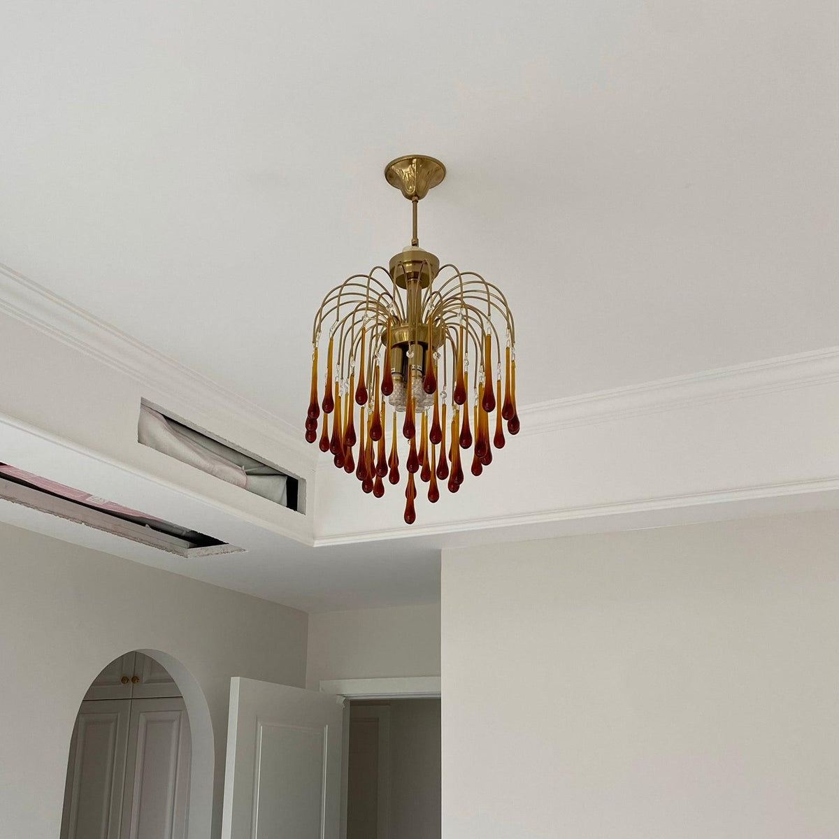 This Clérachic pendant hangs near a ceiling vent in a plain hallway, its caramel crystal drops catching the light.