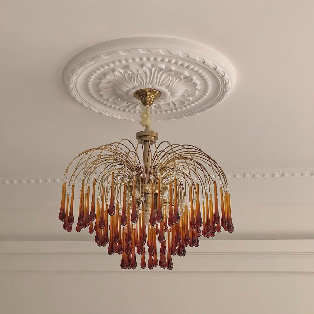 A flush ceiling mount holds this Clérachic chandelier close beneath an ornate plaster medallion, its caramel drops in tiers.