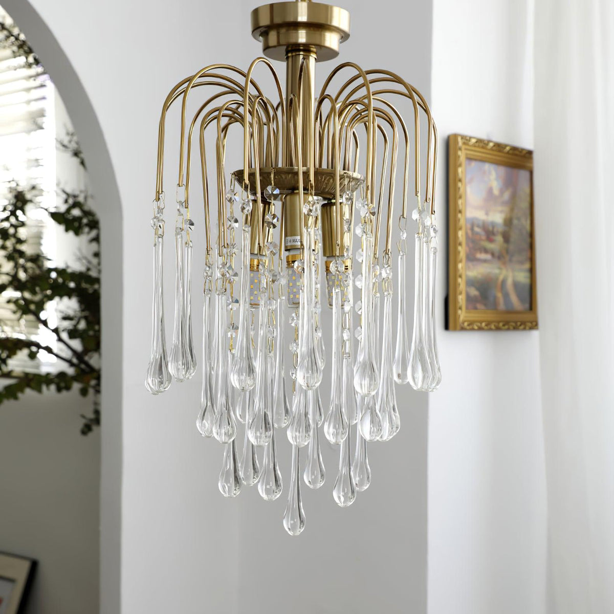 Clear crystal drops on this Clérachic pendant hang near a framed picture beside an arched white doorway.