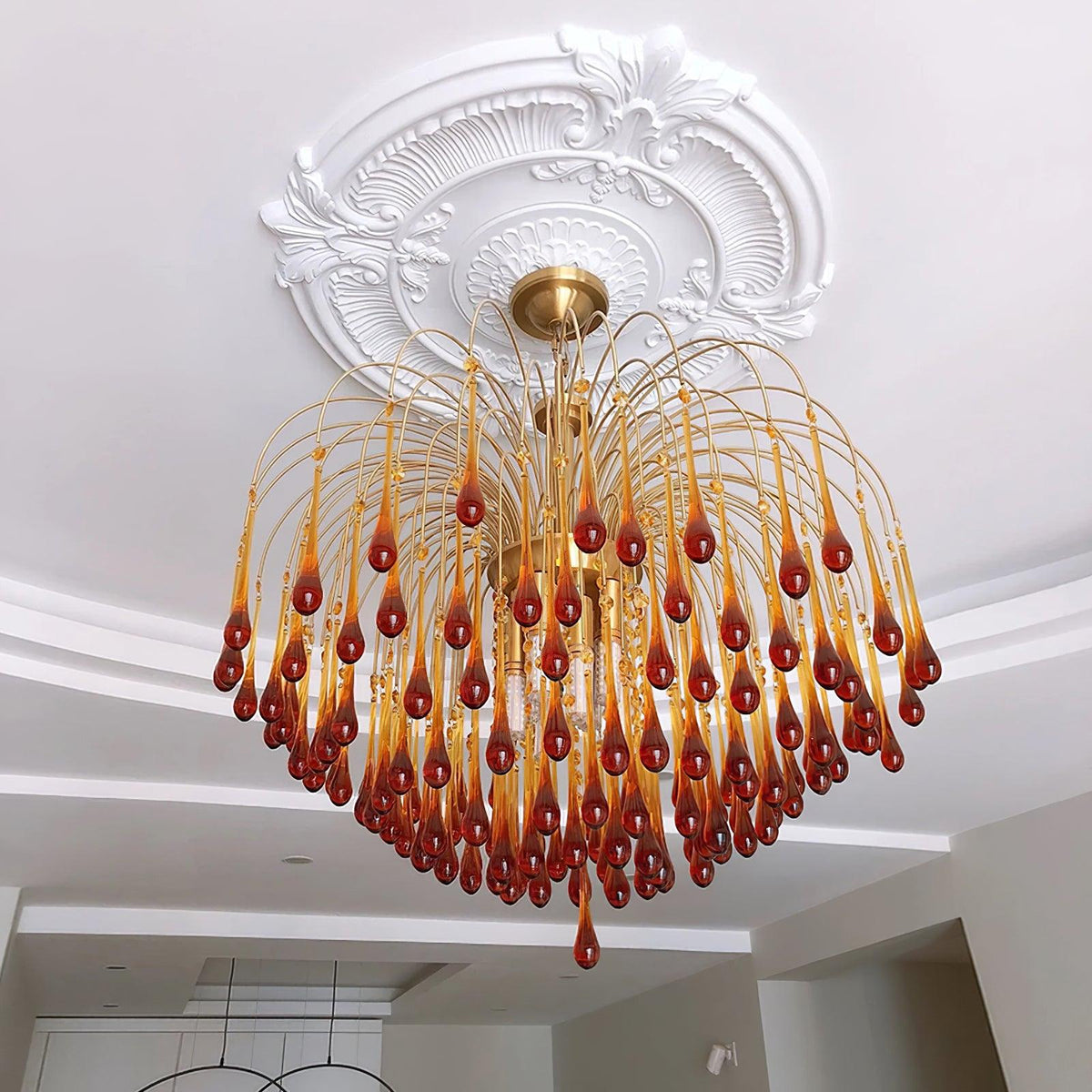 This Clérachic chandelier hangs beneath an ornate ceiling medallion in a hallway with a round mirror on the wall.