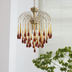 Deep caramel crystal drops on this Clérachic chandelier glow warm above trailing green leaves and pale blinds.