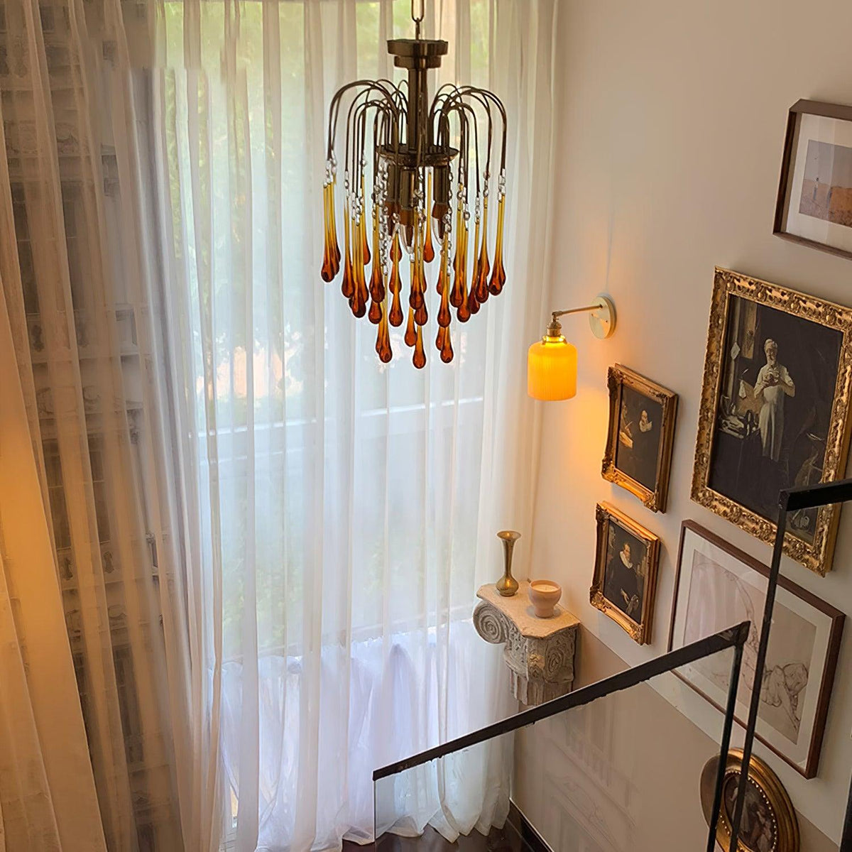 This Clérachic pendant hangs in a stairwell beside a sheer curtain, wall sconce and gilt-framed pictures.