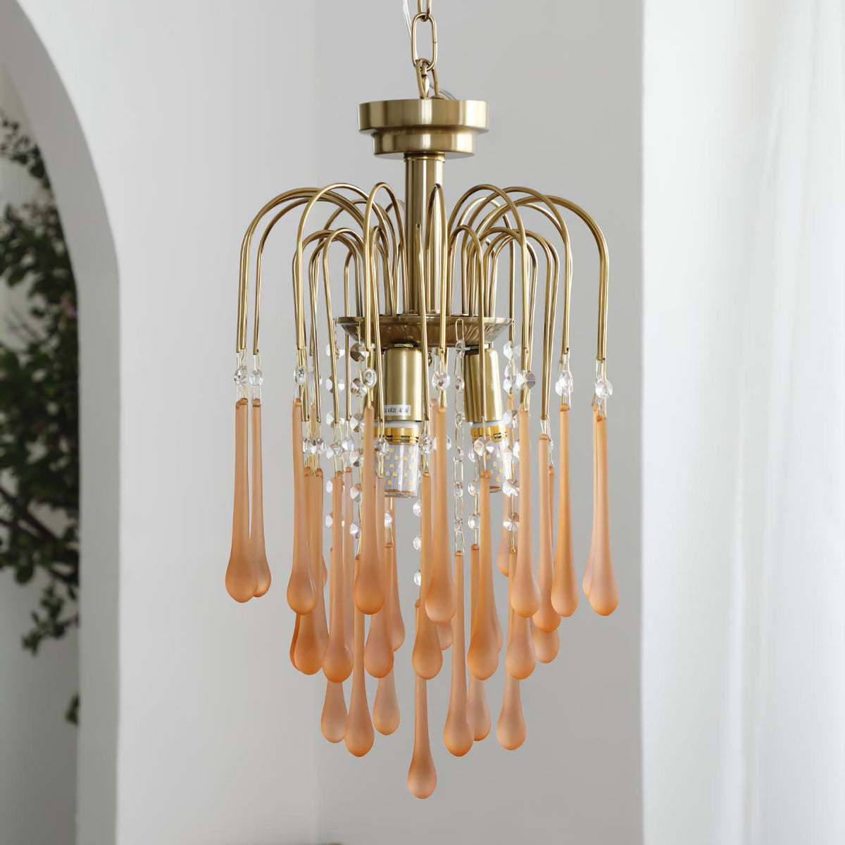 Blush-caramel crystal drops on this Clérachic pendant hang beside a leafy plant on a plain white background.