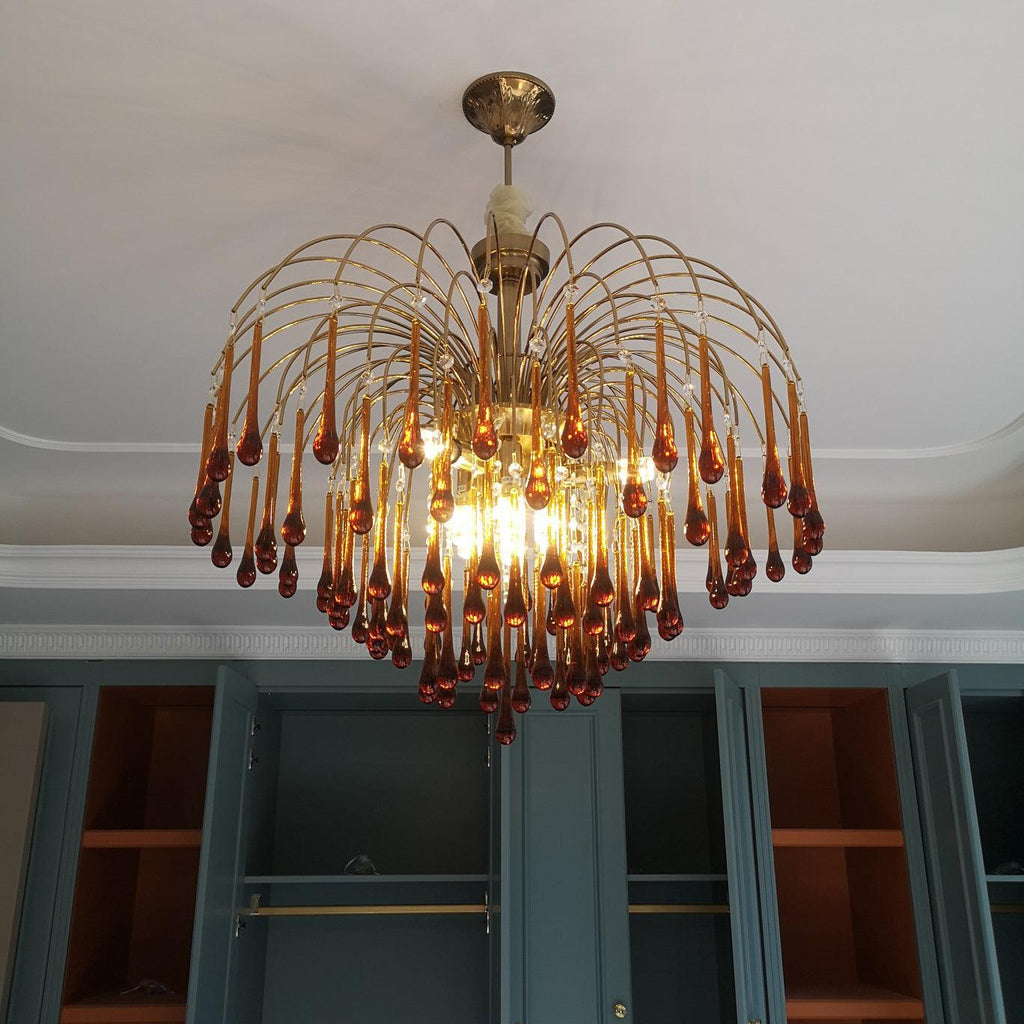 Multiple warm bulbs light this Clérachic chandelier from within, its caramel crystal drops set against dark teal cabinetry.