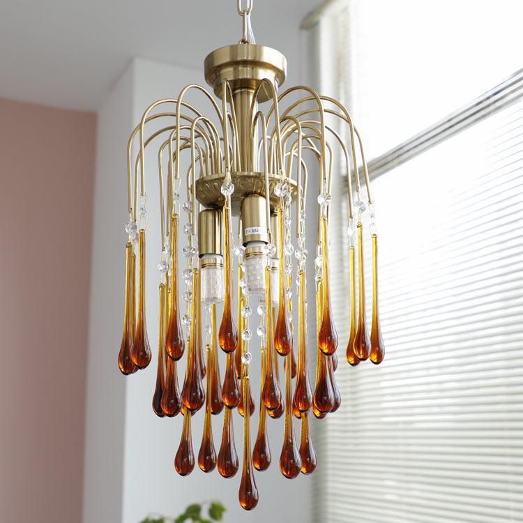 Caramel and clear crystal drops mix on this Clérachic pendant, hung near a window with blinds and a small plant.