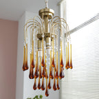 This Clérachic pendant's caramel and clear crystal drops hang beside a window with white blinds, its antique brass body visible.