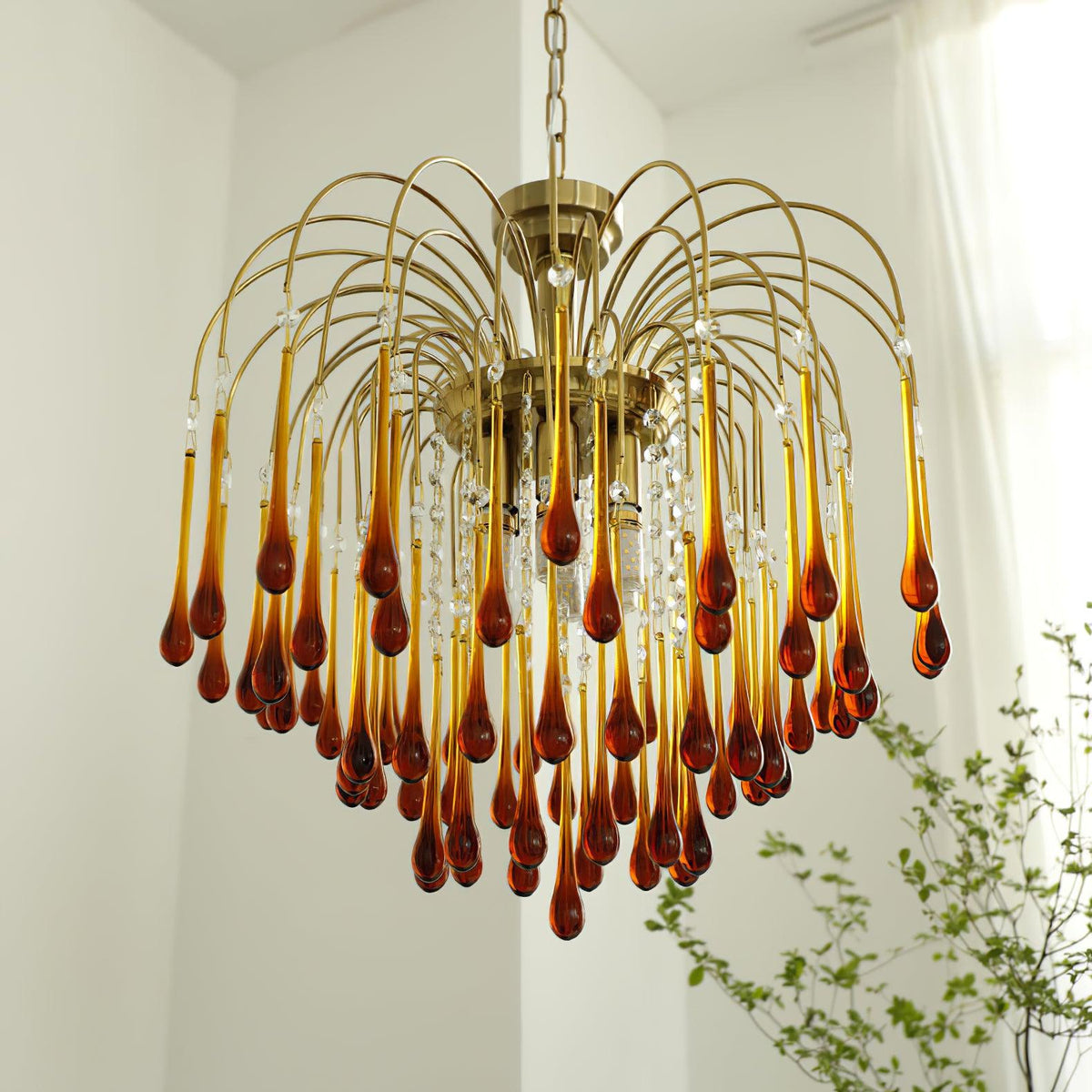 A leafy plant sits beside this Clérachic chandelier, its many caramel crystal drops catching the window light.