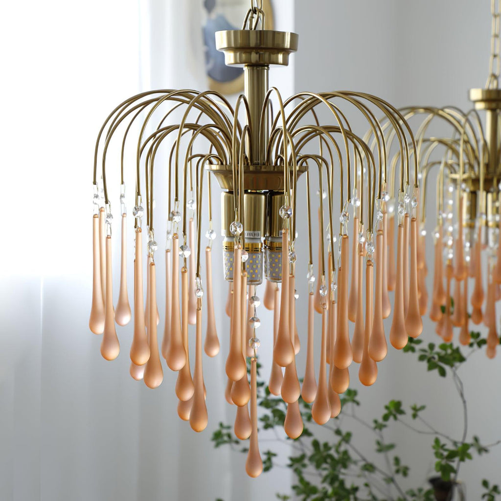 The same blush-caramel crystal drops on this Clérachic chandelier are shown closer, beside a sheer curtain and green plant.