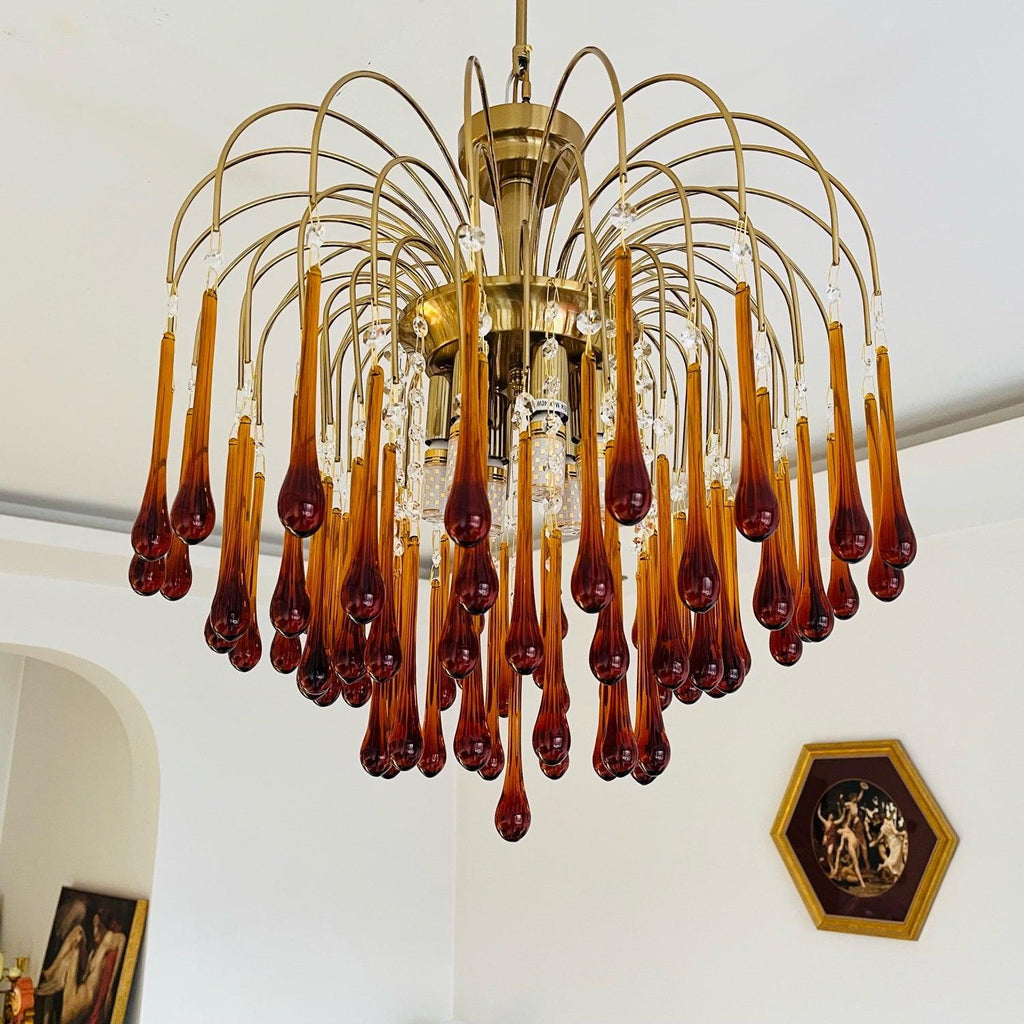 This Clérachic chandelier hangs in an arched alcove, its tiers of caramel crystal drops lit beside a decorative wall plate.