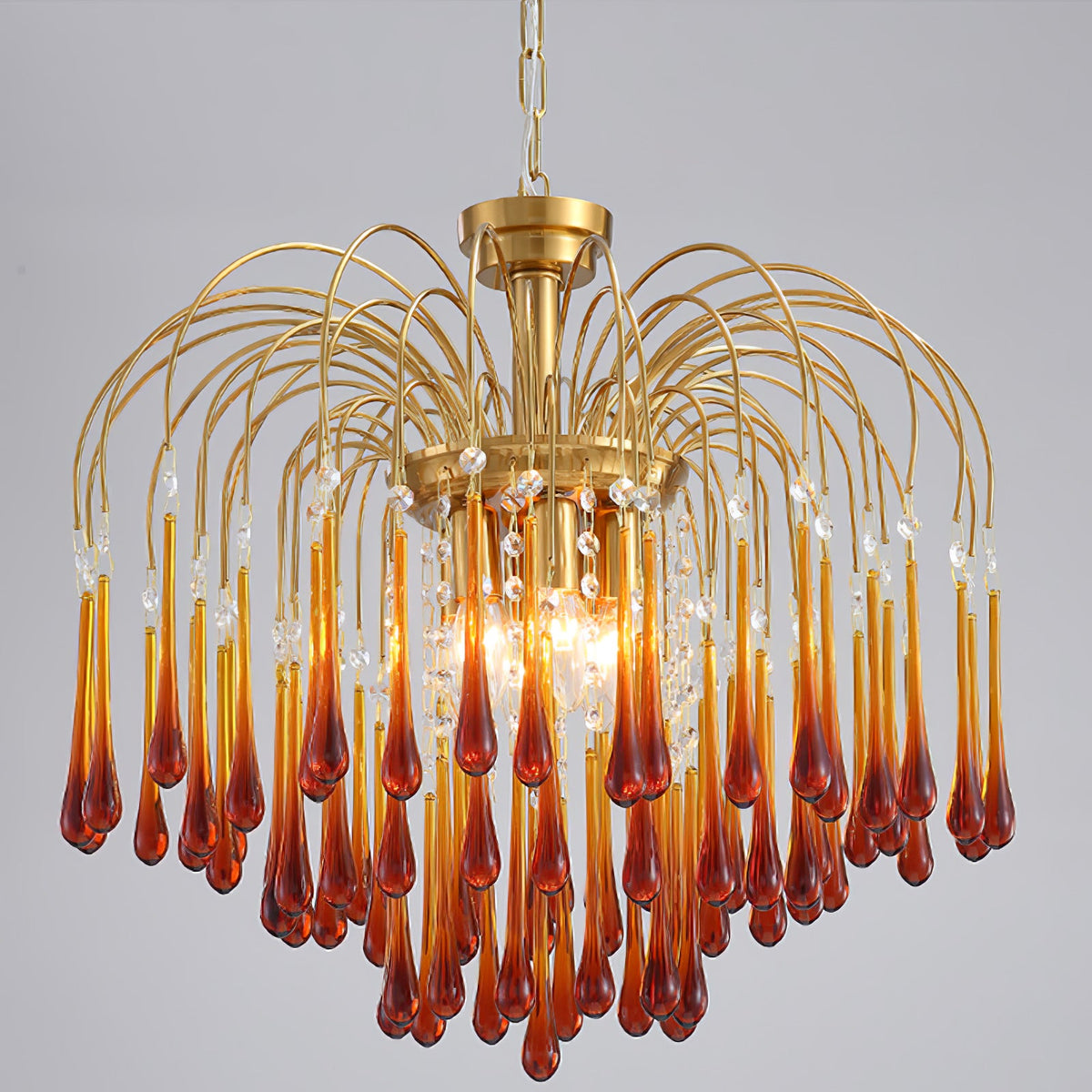 Caramel and clear crystal drops mix on this Clérachic chandelier, lit against a plain dark grey backdrop.