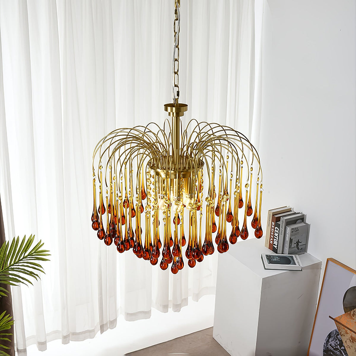 This Clérachic pendant hangs near a sheer curtain, with a small plant and stacked books visible below.