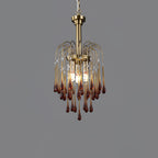 This Clérachic pendant's caramel crystal drops are lit against a dark grey backdrop, brass arms arcing above.