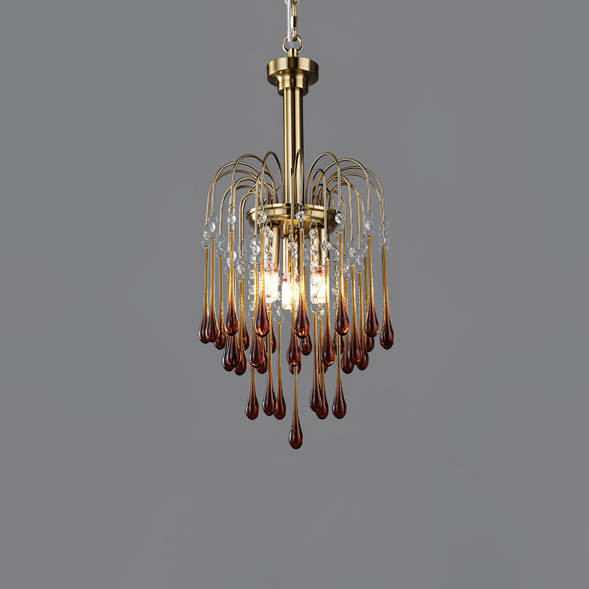 This Clérachic pendant's caramel crystal drops are lit against a dark grey backdrop, brass arms arcing above.