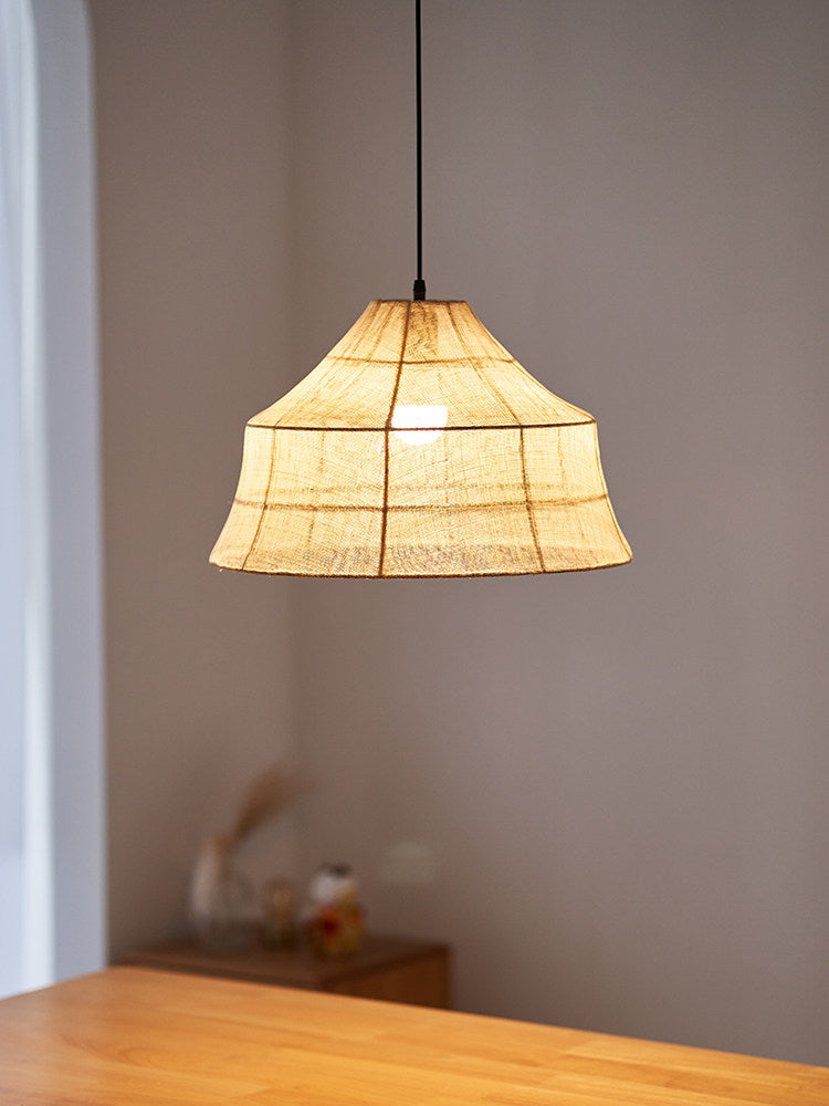 Close view of a lit Clérachic pendant's faceted woven shade, glowing warm above a wooden corner surface.