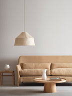An unlit Clérachic pendant hangs above a beige sofa and round coffee table in a neutral living room.