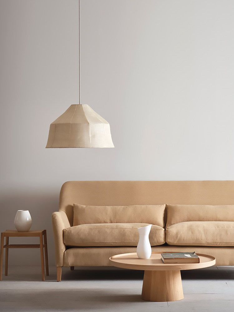 An unlit Clérachic pendant hangs above a beige sofa and round coffee table in a neutral living room.