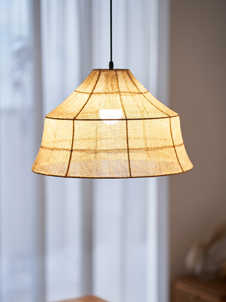 Up close, a lit Clérachic pendant's faceted shade glows warm against a sheer curtain backdrop.