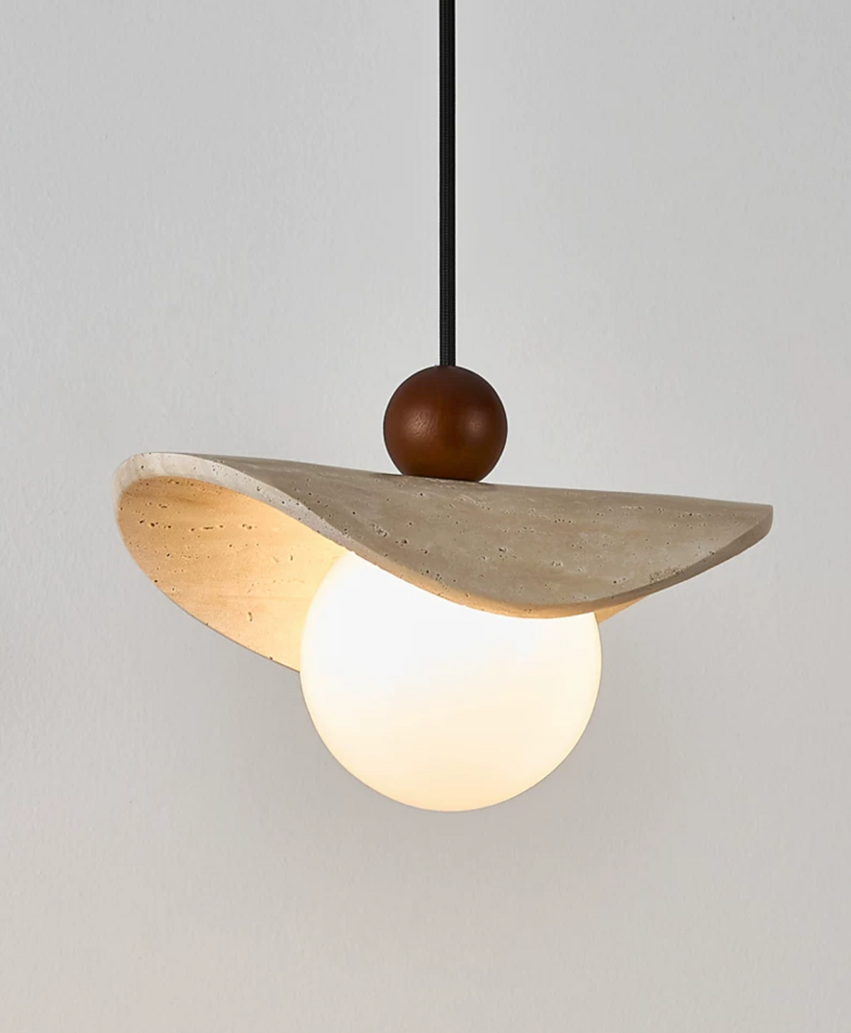 Close view of the curved underside of this Clérachic pendant's travertine sail above its opal globe.