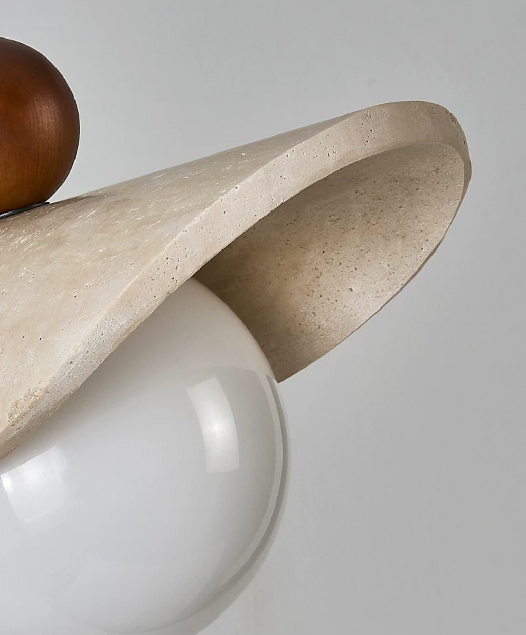 Extreme close view of the travertine sail meeting the opal glass globe on this Clérachic pendant.