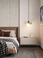 This travertine sail Clérachic pendant lights a bedroom corner beside a leather headboard and framed wall art.