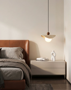 Seen across the room, a travertine sail Clérachic pendant glows beside a leather bed and beige nightstand.