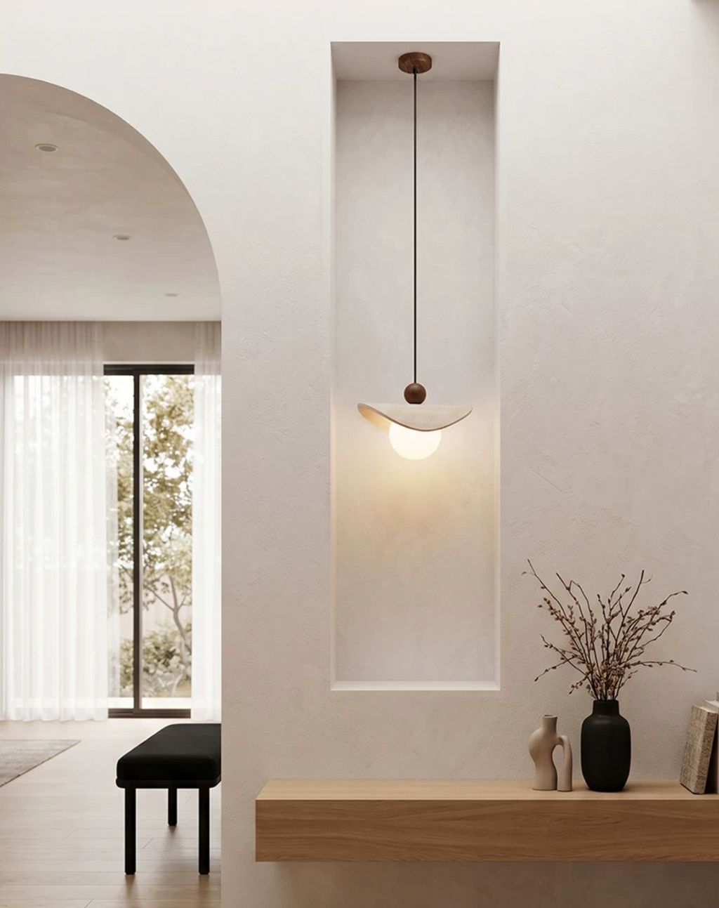 A travertine sail Clérachic pendant glows in a narrow wall niche beside a small vase of branches.
