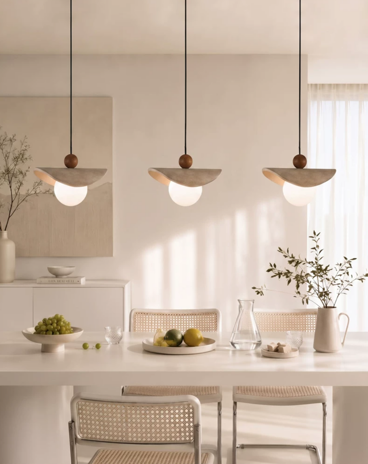 Three travertine sail Clérachic pendants cluster above a kitchen counter set with a bowl of fruit.