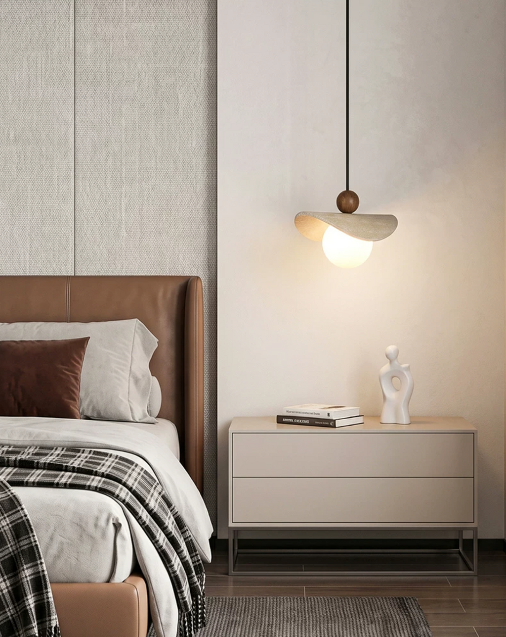 A travertine sail Clérachic pendant glows beside a tan leather headboard, a nightstand holding books and a small sculpture.