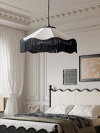 Above a bed with a wrought-iron headboard, this Clérachic pendant glows warm beside sheer curtains.