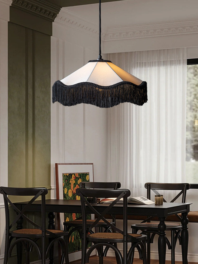 This Clérachic pendant's black fringe skirt glows warm above a dark wood dining table set with black chairs.
