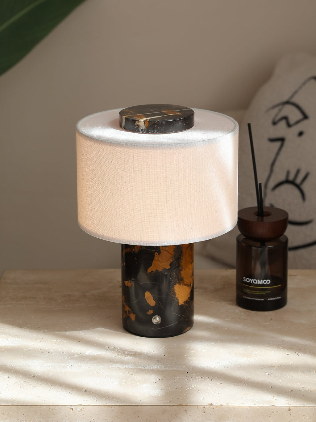Close-up of the Clérachic table lamp's black-and-gold base beside a small diffuser bottle, sunlight casting soft shadows.