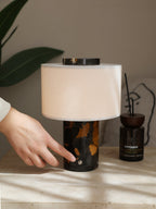 A fingertip presses the touch switch on the Clérachic table lamp's black-and-gold marble base to turn it on.