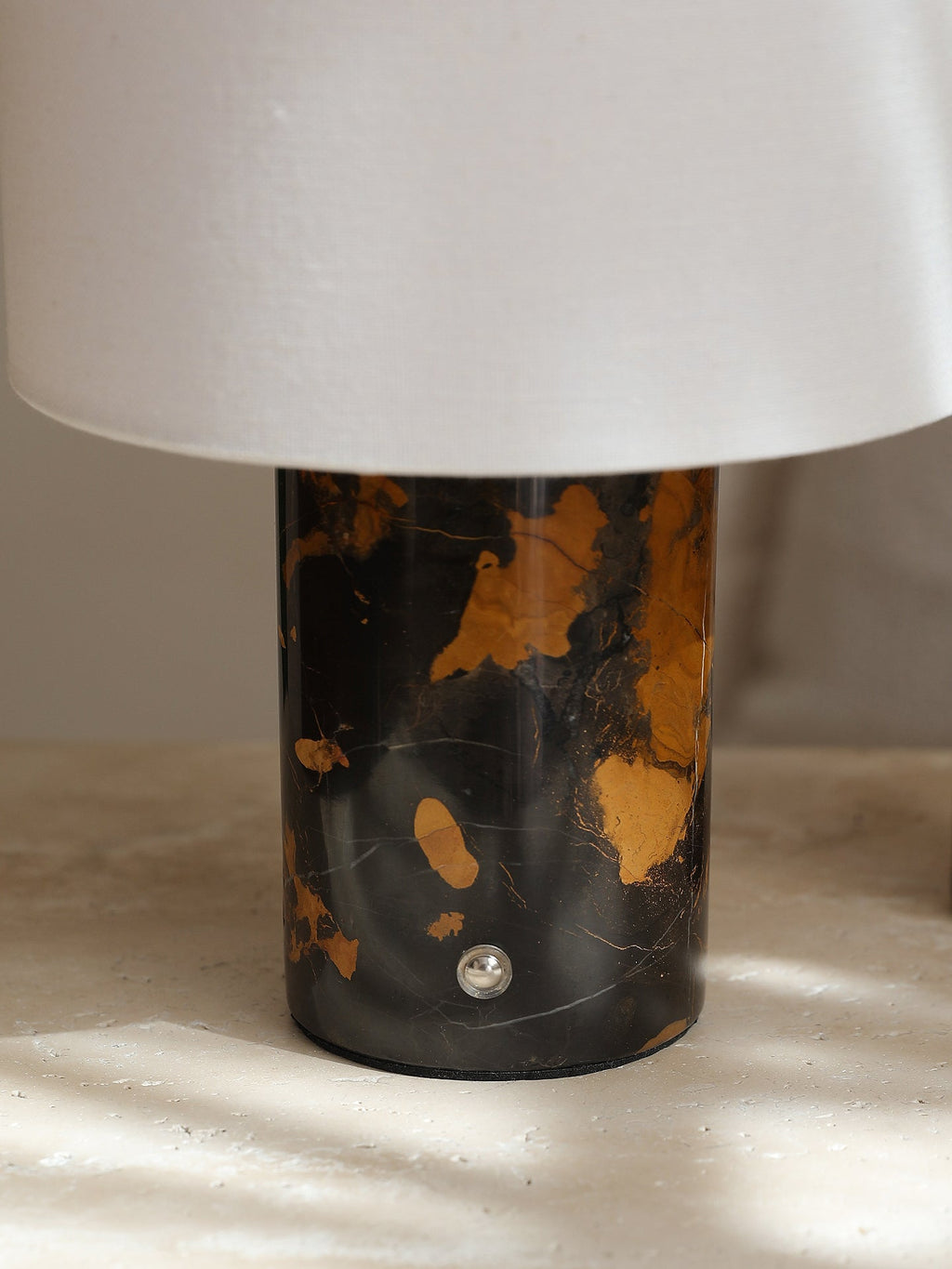 Close-up of the Clérachic table lamp's black-and-gold stone base, its polished surface catching direct sunlight.