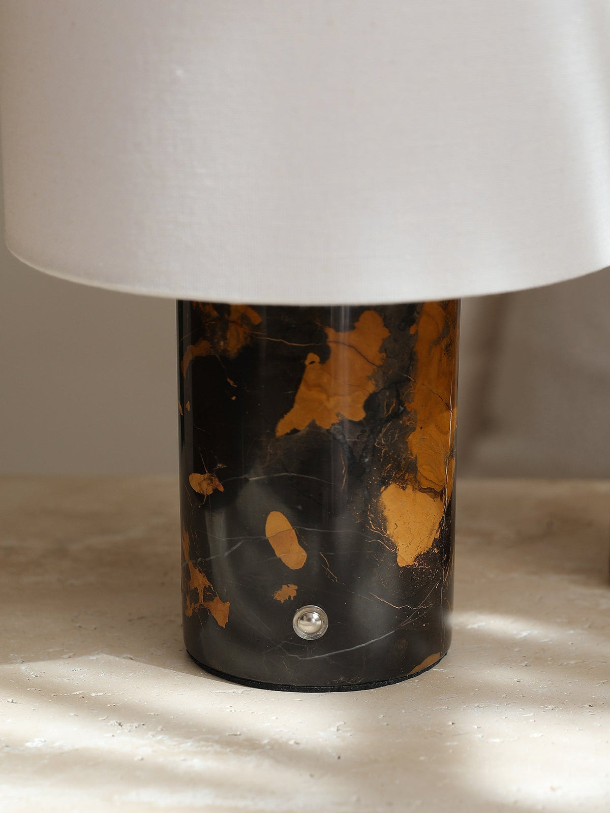 Close-up of the Clérachic table lamp's black-and-gold stone base, its polished surface catching direct sunlight.