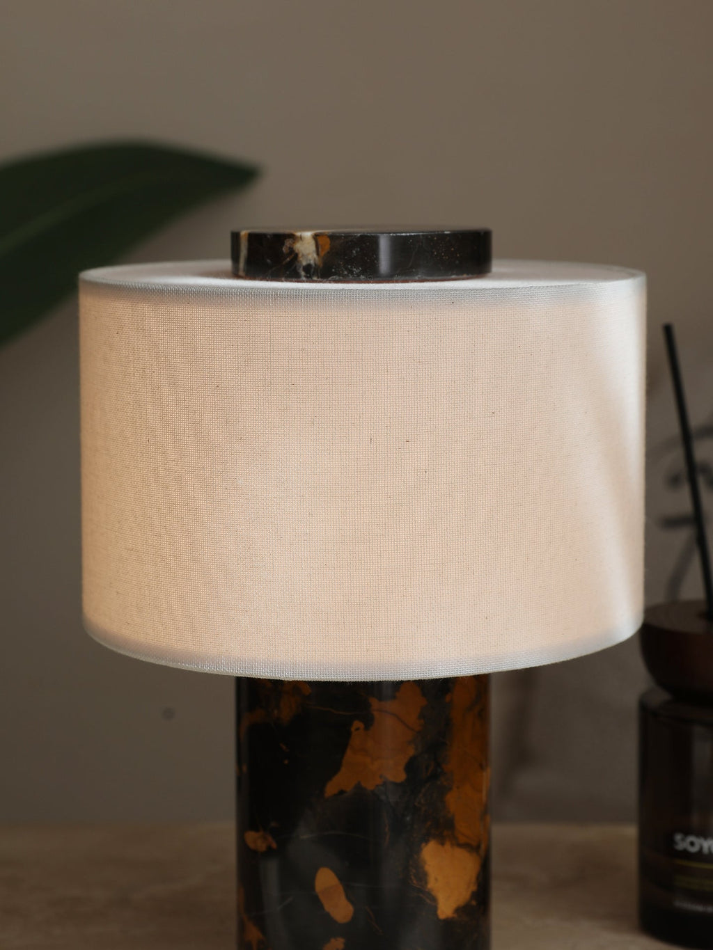 The Clérachic table lamp's black-and-gold stone base stands beside a small dark glass candle jar on a plain surface.