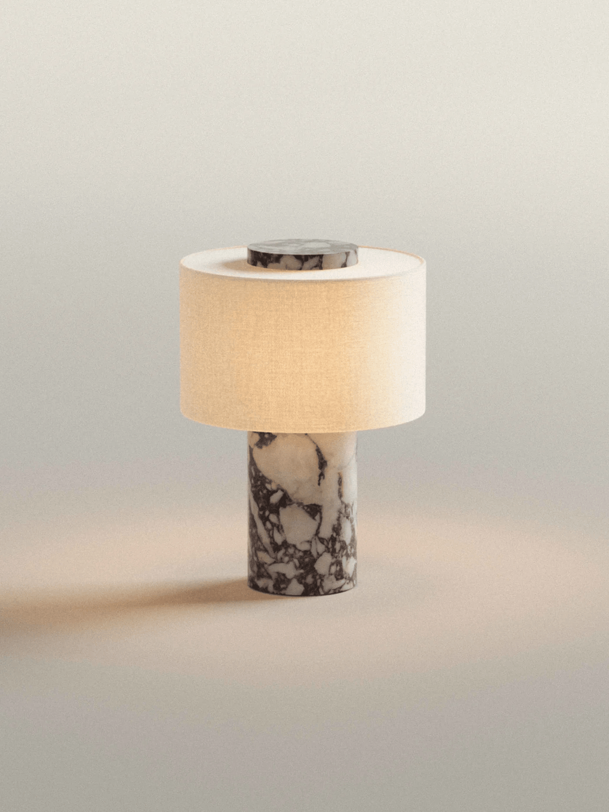 The Clérachic cordless table lamp glows alone against a plain warm-grey backdrop, its white marble base bare of props.