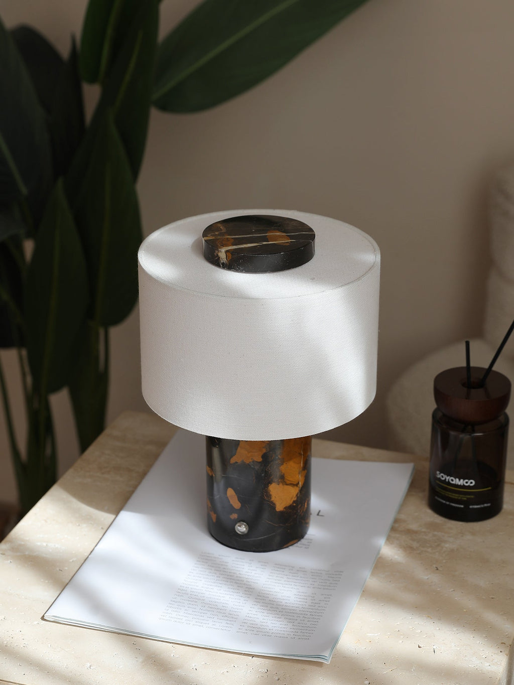 The Clérachic table lamp with its black-and-gold base rests on a folded card beside a small potted plant.