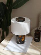 The Clérachic table lamp with its black-and-gold base rests on a folded card beside a small potted plant.