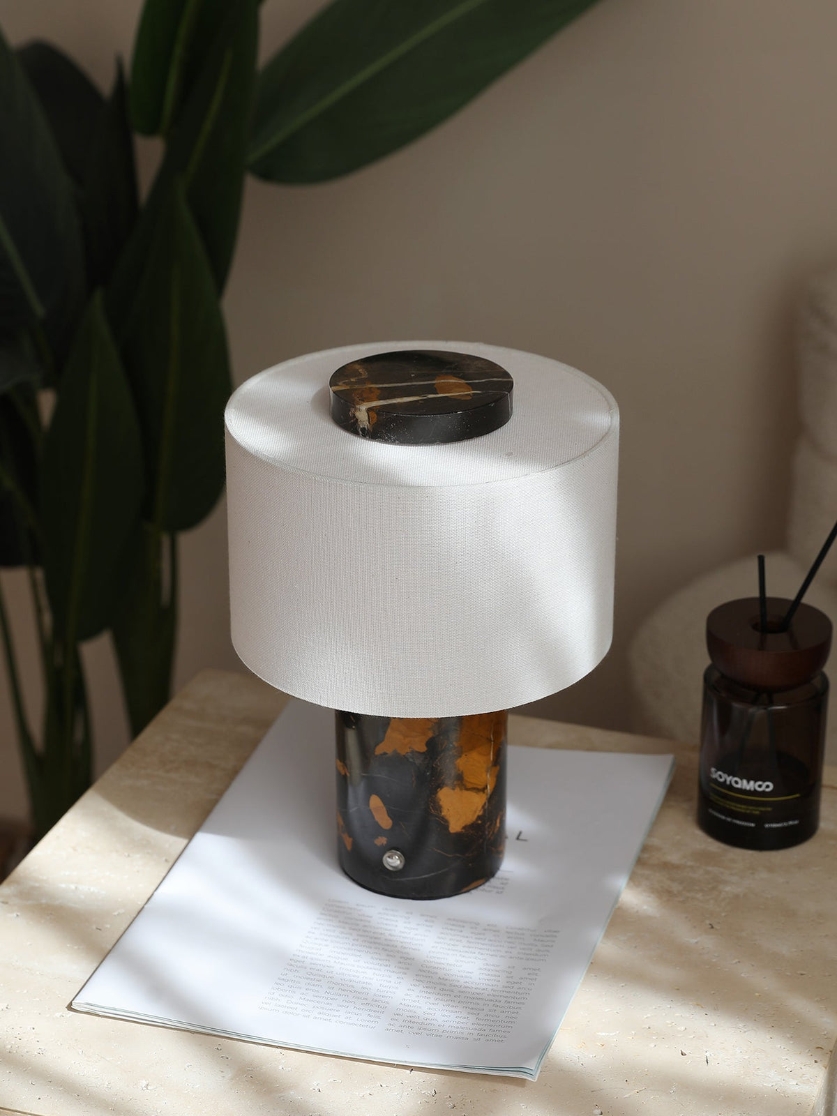 The Clérachic table lamp with its black-and-gold base rests on a folded card beside a small potted plant.