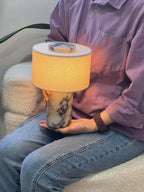 Someone holds the Clérachic cordless table lamp in their lap while seated, showing how light and portable this design is.