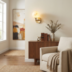 In a hallway lined with framed art, this Clérachic sconce's brass finish lights a corner beside an upholstered armchair and credenza.