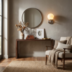 Beneath a round mirror in a sunlit corner, this Clérachic sconce's brass finish glows above a wood console table.